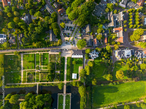 Aerial view of townv residential zone with trees, central parking and public buildings, formal garden with geometric paths, canal and bridge, blending urban planning with green space symmetry.