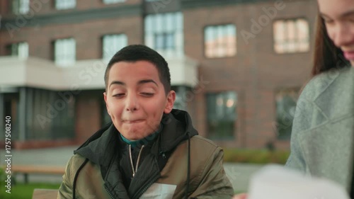 Boy laughs in surprise as aunt makes mistake during playful moment, both smiling warmly outdoors near building background, capturing joy, family bonding, and candid reaction of shared happiness