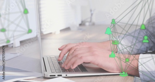 Typing male hands pressing laptop keys at office desk, displaying papers, green network icons