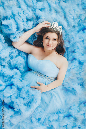 pregnant girl lies on a blue background. girl in a blue dress. girl with a diamond crown. High quality photo
