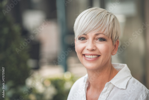 Closeup face of european happy blond adult woman. Smiling face of beautiful mid aged female person dressed in white summer shirt.