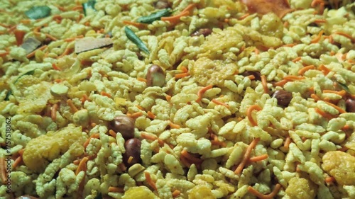 A large, round metal dish is filled with a flavorful Indian snack mix known as namkeen. The golden-colored mixture appears to contain flattened rice, peanuts, and other crispy tidbits.