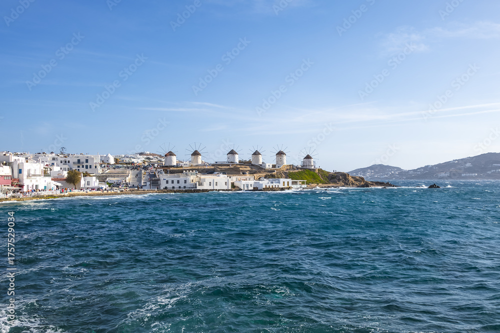 Fototapeta premium scenic view of famous windmills in Chora, Mykonos, Greece. Greek landmark. view of Mykonos Island from the water. deep blue