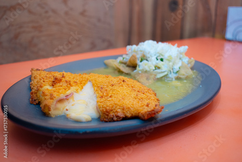 Imagen horizontal de un plato de milanesa de pollo empanizada rellena de queso y jamon acompañada de chilaquiles verdes