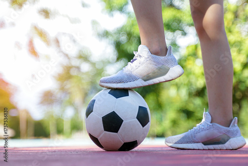 A person in white running shoes steps on a classic black and white soccer ball on a sports court.