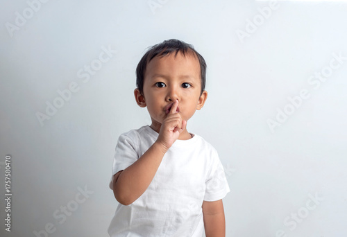 Asian boy doing a Please Keep Quiet gesture towards the camera. Studio shot with white background.
