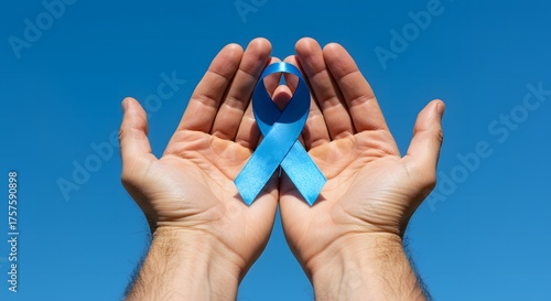 Close-up shows a person's hands holding and offering a light blue ribbon against a blue background.