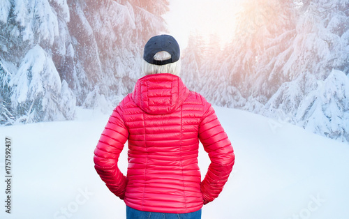 Rear view of blond woman wearing a cap standing and admiring winter landscape in  forest scene.