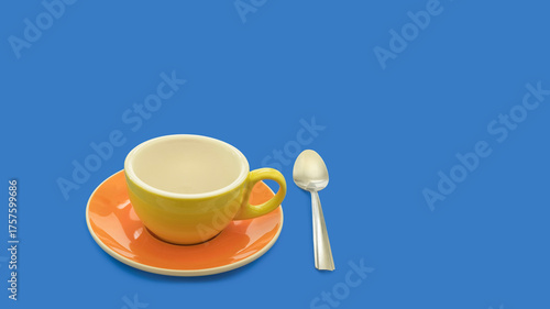 Close-up of a colorful porcelain coffee cup, saucer, and spoon, on a blue background with enough copy space for a calendar, card, or poster.