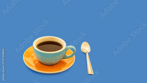 Close-up of a colorful porcelain coffee cup, saucer, and spoon, on a blue background with enough copy space for a calendar, card, or poster.