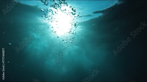 An underwater view looking up towards the sun with a stream of air bubbles rising to the surface