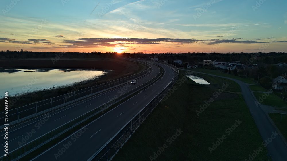 Fototapeta premium Car Driving on Curved Highway at Sunset by Lake.