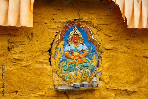 Colorful carved painting of a Buddhist deity on a yellow wall inside Tradruk Temple, a sacred site in Tsetang, Lhoka (Shannan), Tibet, showcasing traditional Tibetan art and devotion.