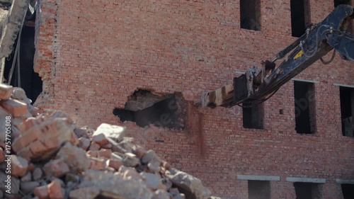 Excavator demolishing brick wall of old building