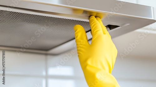 Gloved hand cleaning a range hood filter. Ensuring a clean and efficient kitchen with protective gear. Simple maintenance for a healthy home. Bright yellow glove.