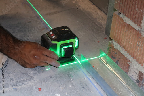 Green Cross-Line Laser Level Tool in Worker's Hand on Construction Site.