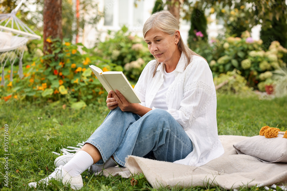 © New Africa - Senior woman reading book on blanket in garden