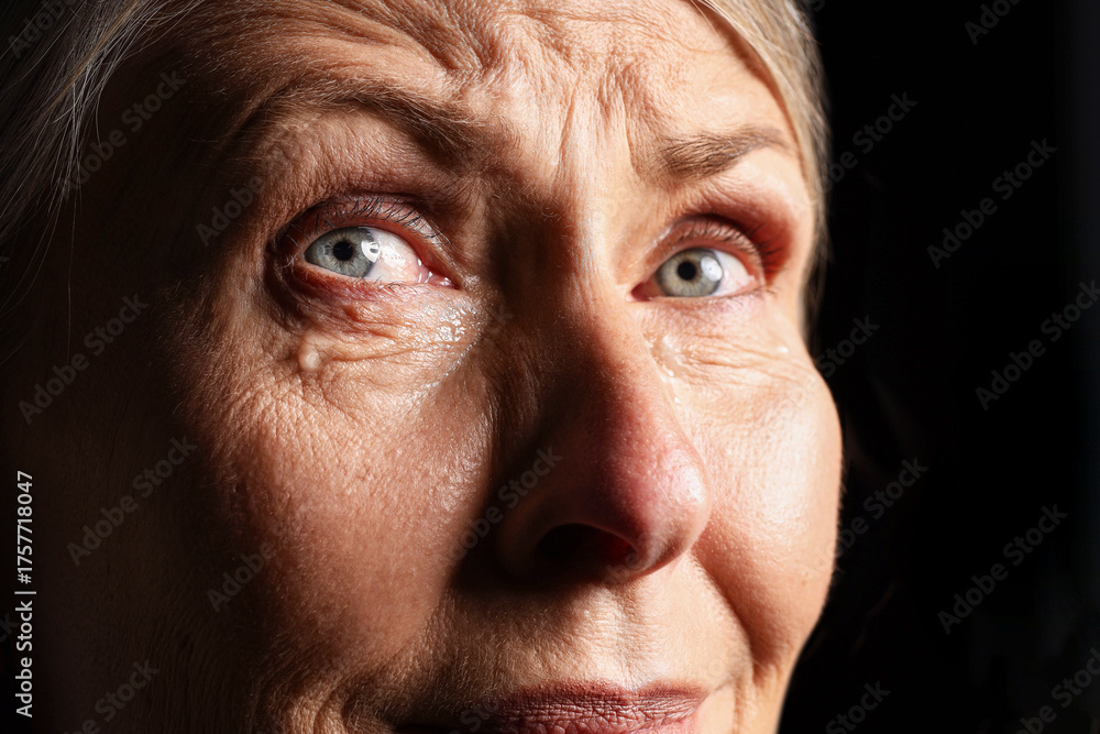 Obraz premium Senior woman crying on black background, closeup