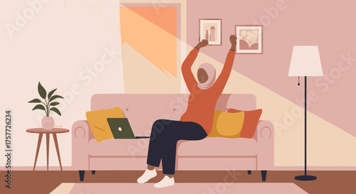 A joyful woman in a hijab celebrates success, raising her arms in triumph while working on her laptop from her cozy, sunlit living room.