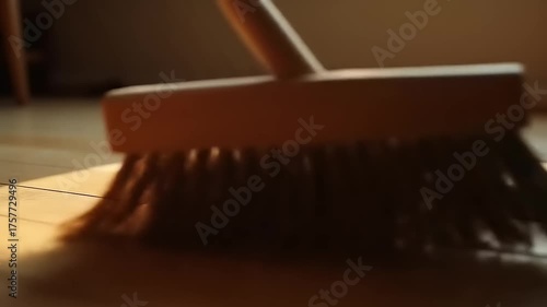 Broom sweeping wooden floor with cleaning dust.