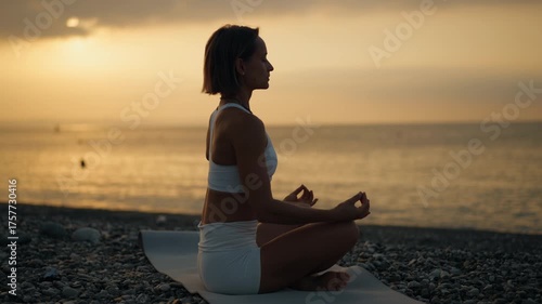 Young woman practices yoga on a mat by the sea during a peaceful morning sunrise. She sits in a meditative posture facing the water. Concept of mindfulness, inner balance, and connection with nature