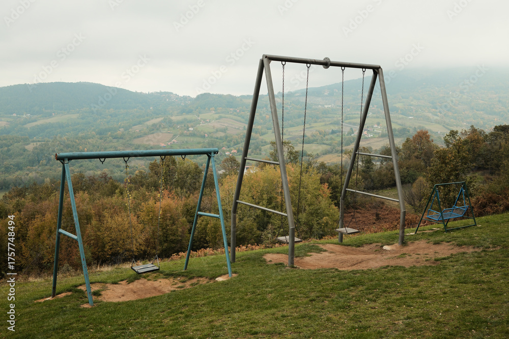 Fototapeta premium Multiple swings placed on a hill with a panoramic view of mountains and valleys under cloudy sky. Ideal for travel, recreation, and freedom concepts