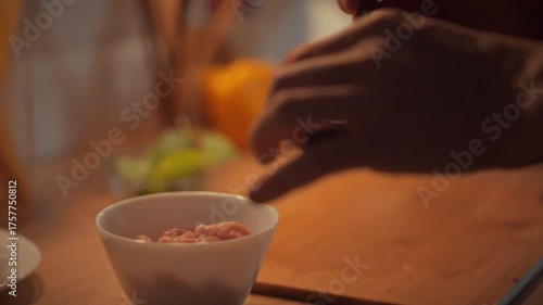 A person adds soy sauce to a bowl of chicken meat to create a marinade. This activity takes place in a warm kitchen, highlighting the process of preparing a meal