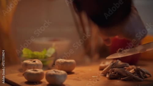 In a warm kitchen, a person skillfully slices fresh mushrooms on a wooden cutting board. Person slicing mushrooms in a cozy kitchen preparation scene during evening cooking time