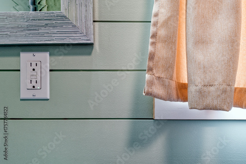 A GFCI electrical outlet in a bathroom next to a curtained window