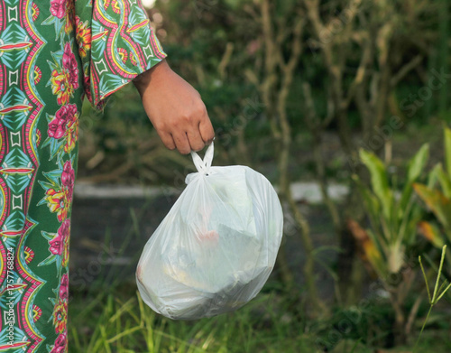 Hand holding a full black plastic trash in outdoor	
