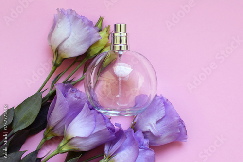 One round perfume bottle with purple eustoma flowers on pink background, top view