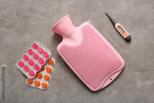 Photography Hot water bottle with different pills and thermometer on grey background