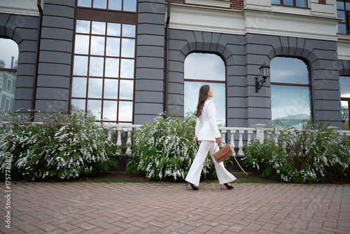 Elegant Businesswoman in White Suit Walking by Modern Building