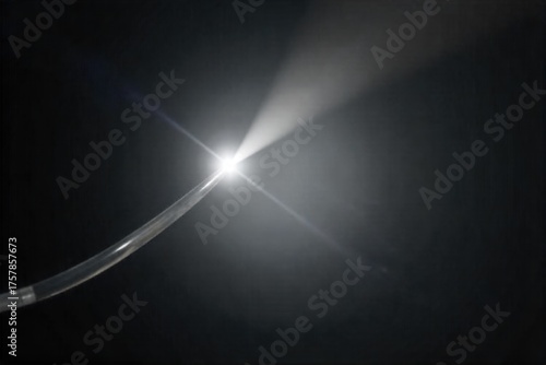 Single Optical Fiber with a Bright, Focused Light Beam Macro shot of a single, transparent optical fiber with a sharp, intense beam of pure white light emanating from its tip. The background is