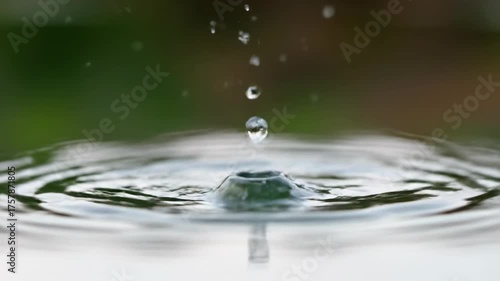 Mesmerizing slow motion close-up of crystal clear water drops gracefully falling and creating intricate ripples in a calm, reflective pond surface splash, slow motion, gracefully falling