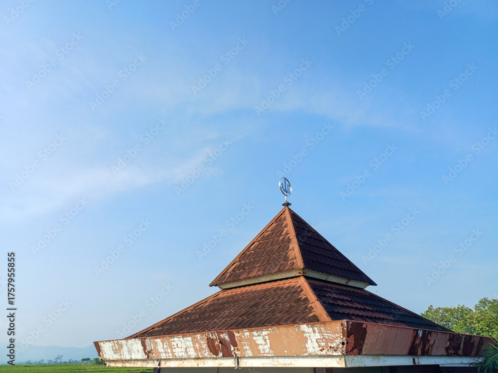 Obraz premium Bright morning view of a simple mosque roof and dome against a clear blue sky in Indonesia, Southeast Asia. Focus on peace, spirituality, Islamic culture, and morning light.