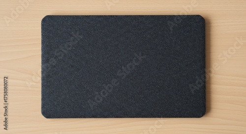 A dark grey felt mousepad with rounded corners placed on a wooden desk surface for commercial usage and mockups