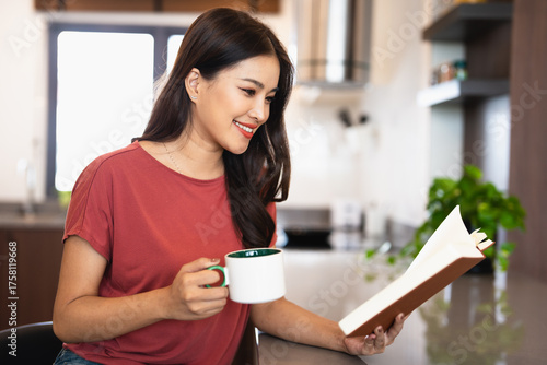 Canvastavla Young woman drinking tea and reading book in her kitchen while enjoying morning at home