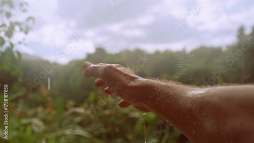 Slow Motion Scene of Outstretched Wet Hand in Rain with Forest and Clouds in Soft Background, Warm Light, Connection with Nature Concept