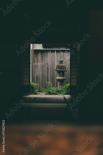 Traditional Japanese courtyard garden viewed from inside a tatami room, featuring a stone lantern and wooden fence