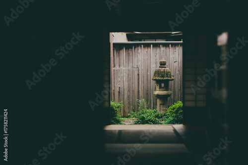 Traditional Japanese courtyard garden viewed from inside a tatami room, featuring a stone lantern and wooden fence