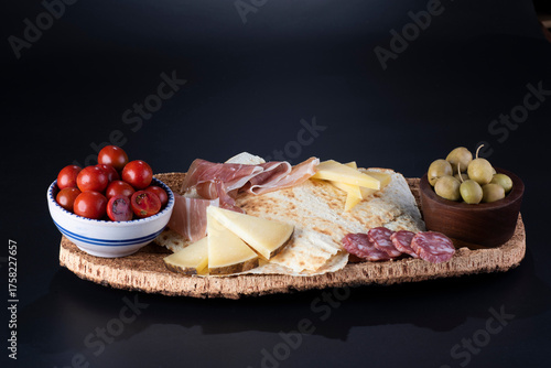 pane carasau con salame, formaggio e olive su vassoio in sughero sfondo nero