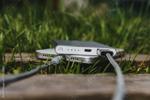 An external battery with charging cables charges a modern smartphone on a wooden surface.
