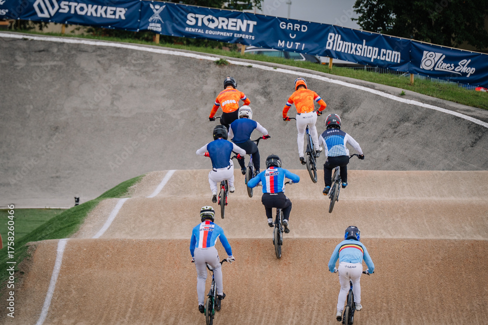 Naklejka premium Valmiera, Latvia - July 12, 2025: BMX racers competing on track with vibrant colors and dynamic motion in the background. BMX European championships