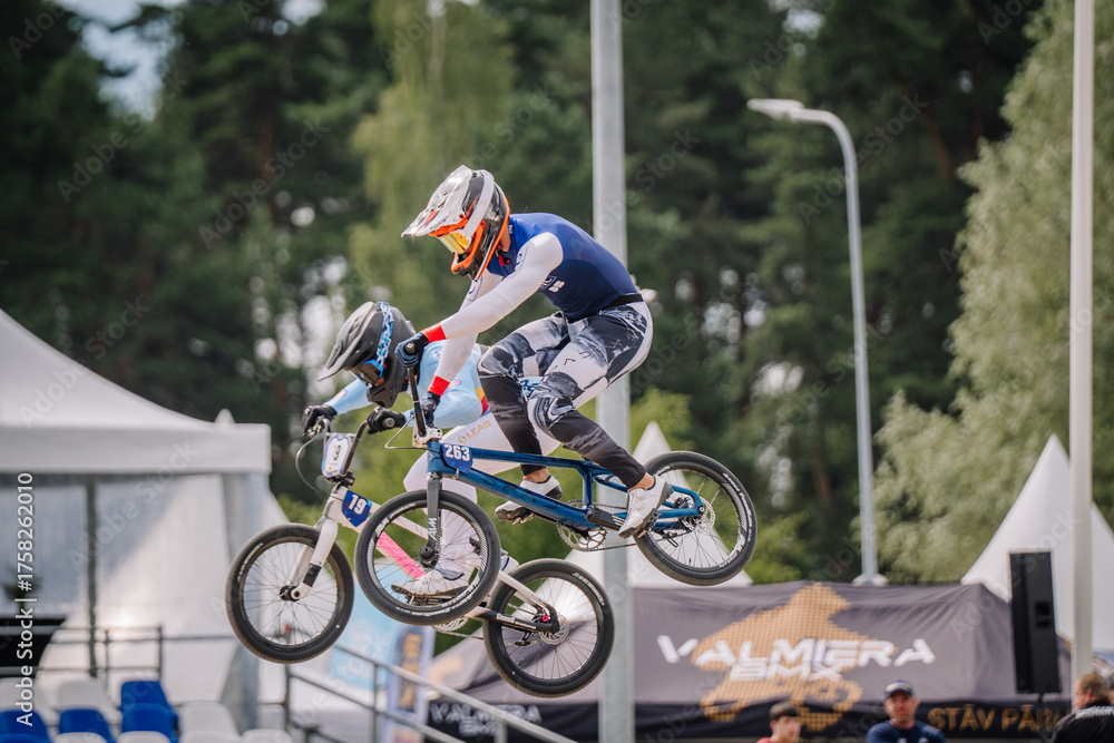 Naklejka premium Valmiera, Latvia - July 12, 2025: BMX rider performing a jump at a cycling event with spectators in background. BMX European championships
