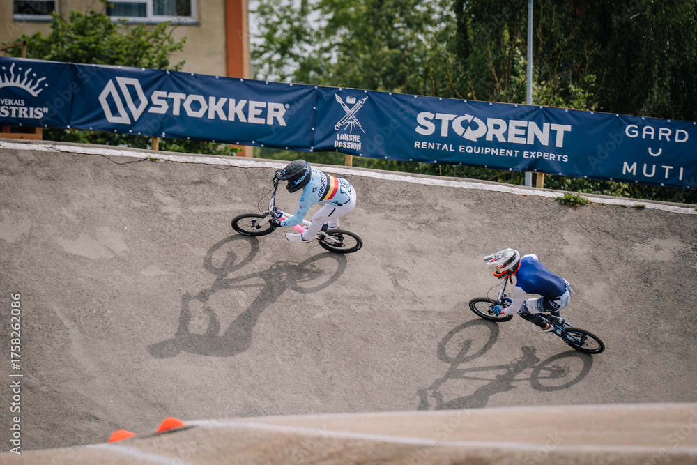 Fototapeta premium Valmiera, Latvia - July 12, 2025: BMX racers competing on track with Stokker and Storen banners in background. BMX European championships