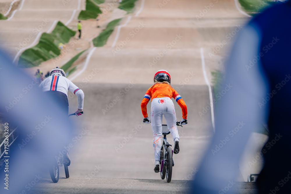 Naklejka premium Valmiera, Latvia - July 12, 2025: BMX racers competing on track with vibrant colors and dynamic motion in background. BMX European championships