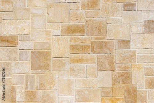 Background or texture of a wall with horizontal masonry of rectangular blocks of sandstone or limestone in beige and golden colors with a thin line of cement mortar, natural building material