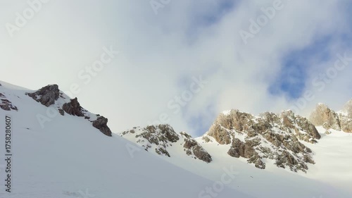 Snow-covered mountain peaks emerging through clouds under a bright winter sky.