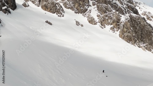 Mountaineer climbing a snowy couloir between steep rocky walls in winter conditions.